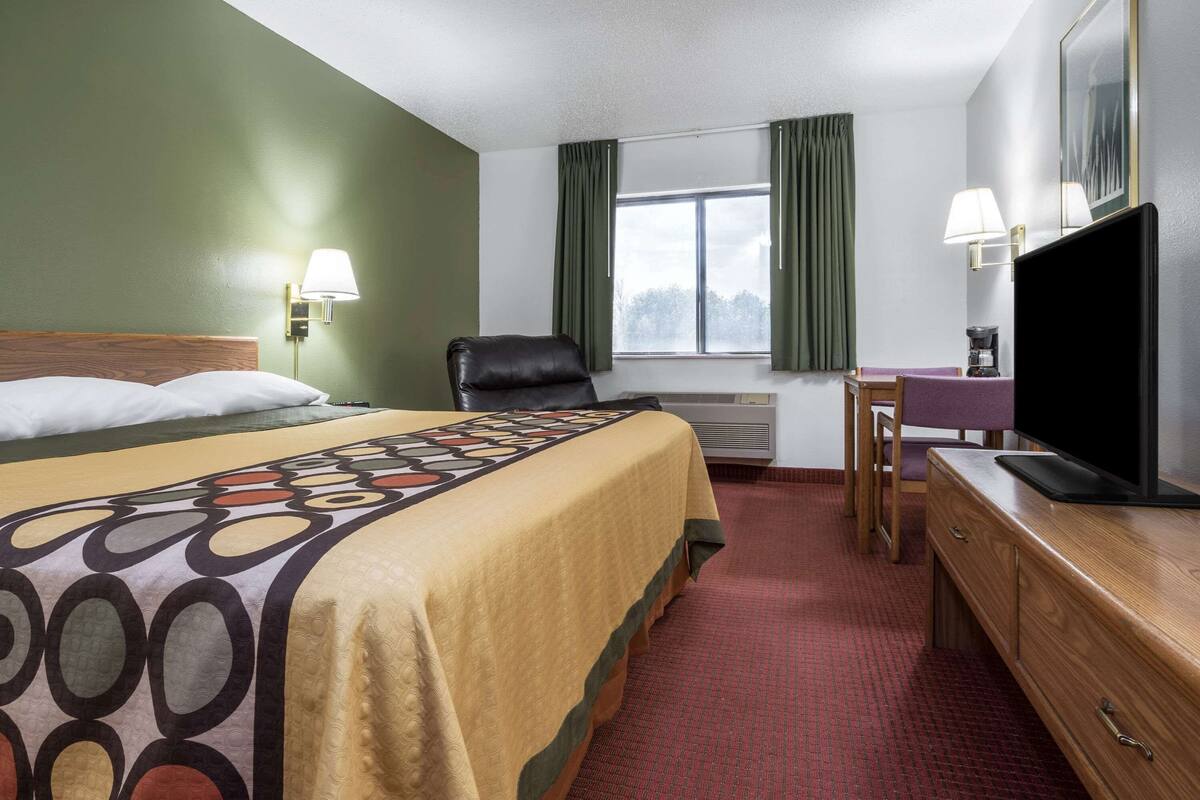 Een hotelkamer met een bed, een bureau, een stoel, een televisie en een raam met gordijnen.