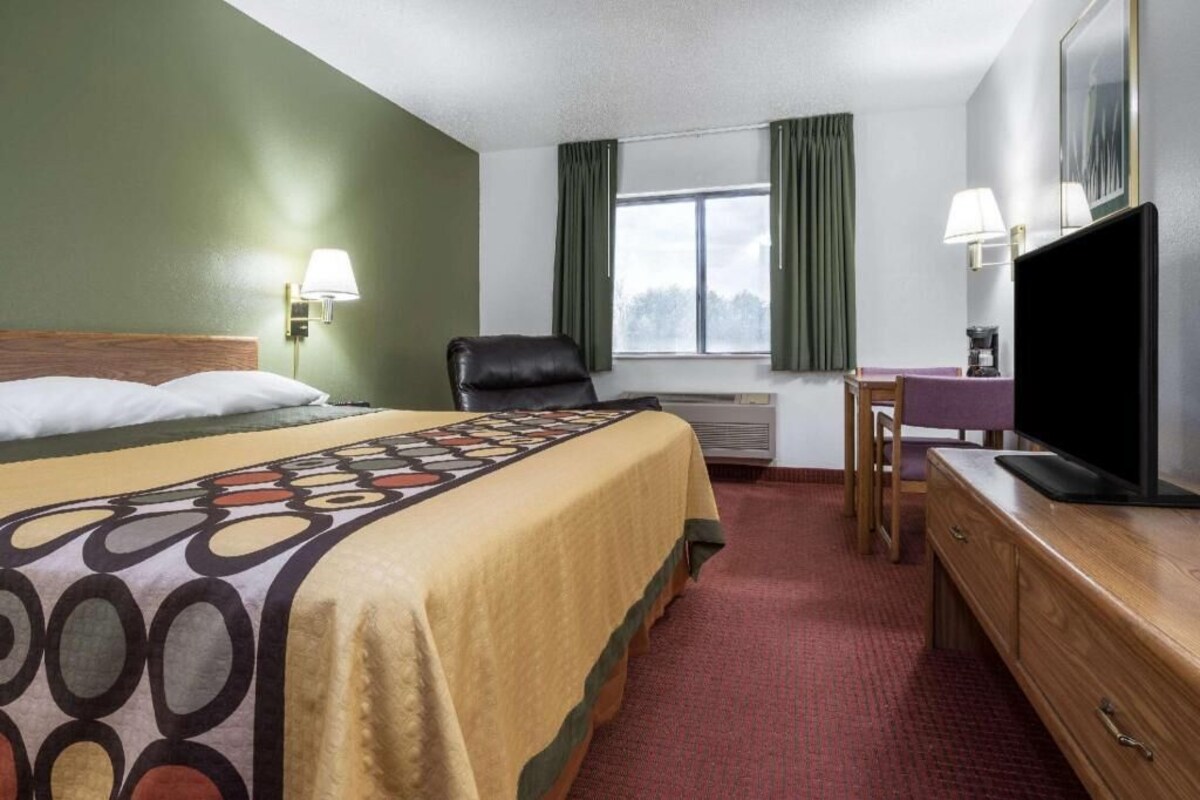 Habitació d'hotel amb llit, escriptori, cadira, televisió i finestra amb cortines.