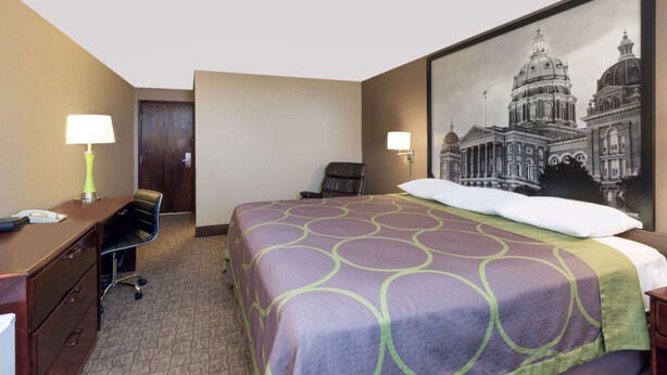 A hotel room with a large bed, a desk with a lamp, a chair, and a framed picture of a building on the wall. - Super 8 by Wyndham Carroll (Carroll)