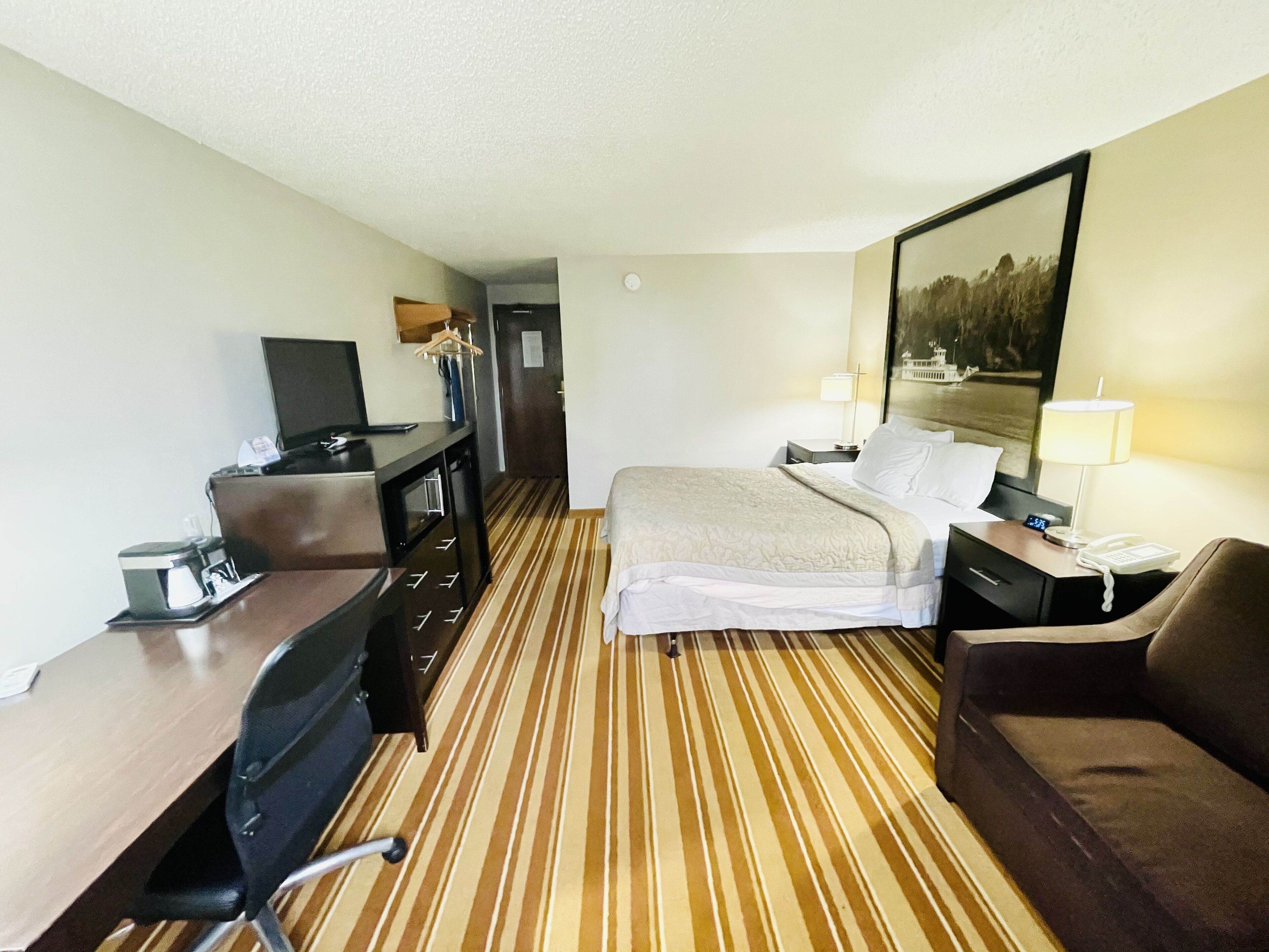 Habitación de hotel con cama, escritorio con computadora, silla, sofá y televisor.