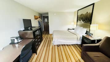 Habitación de hotel con cama, escritorio con computadora, silla, sofá y televisor.