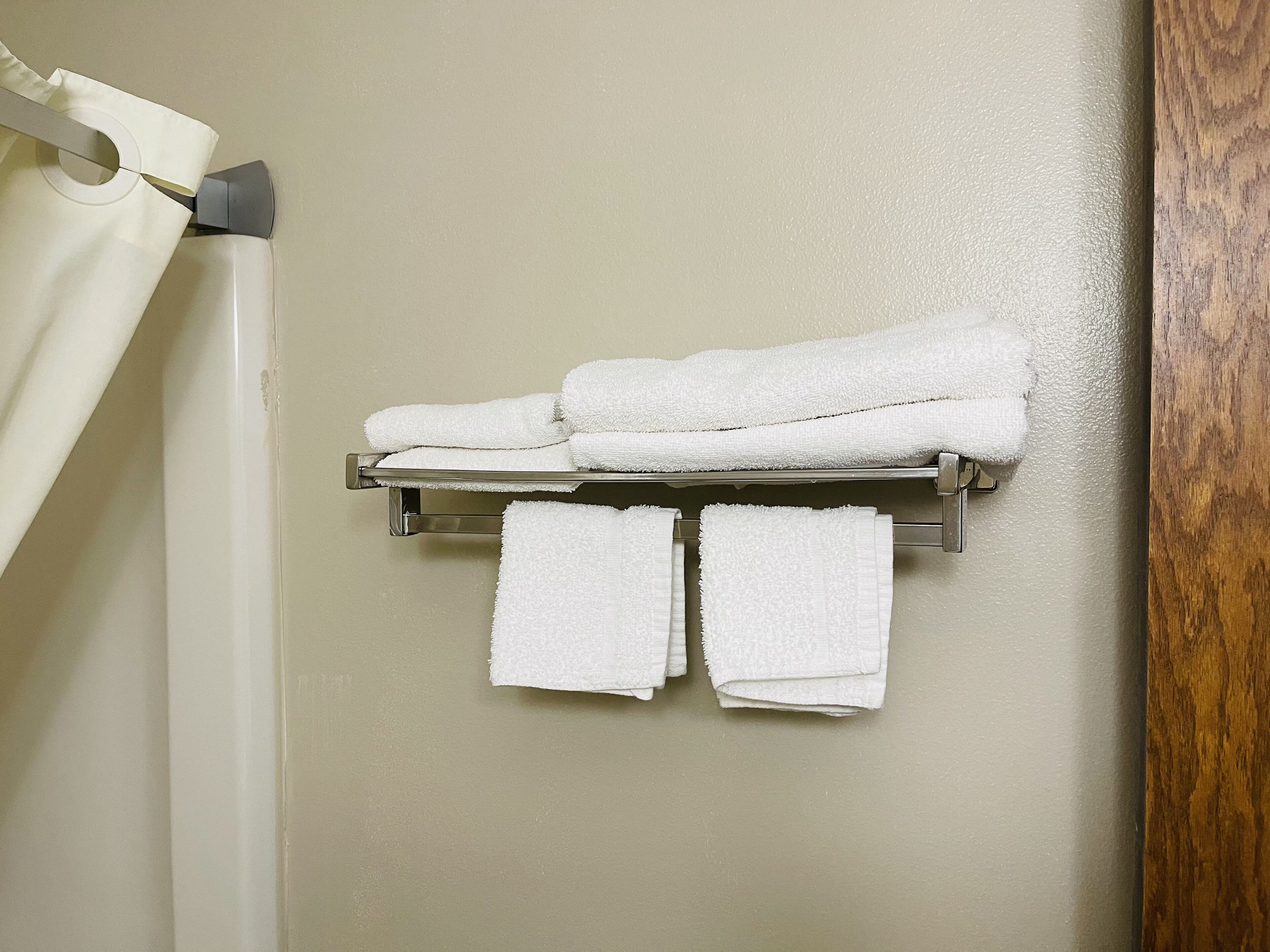 Un baño con un perchero que sostiene tres toallas dobladas y una cortina de ducha.
