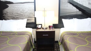 Een hotelkamer met twee bedden, een nachtkastje met een lamp, een telefoon en een wekker.