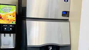 Een roestvrijstalen drankdispenser met een waterkoeler en koffiezetapparaat, geplaatst naast een kast met een potplant erop.