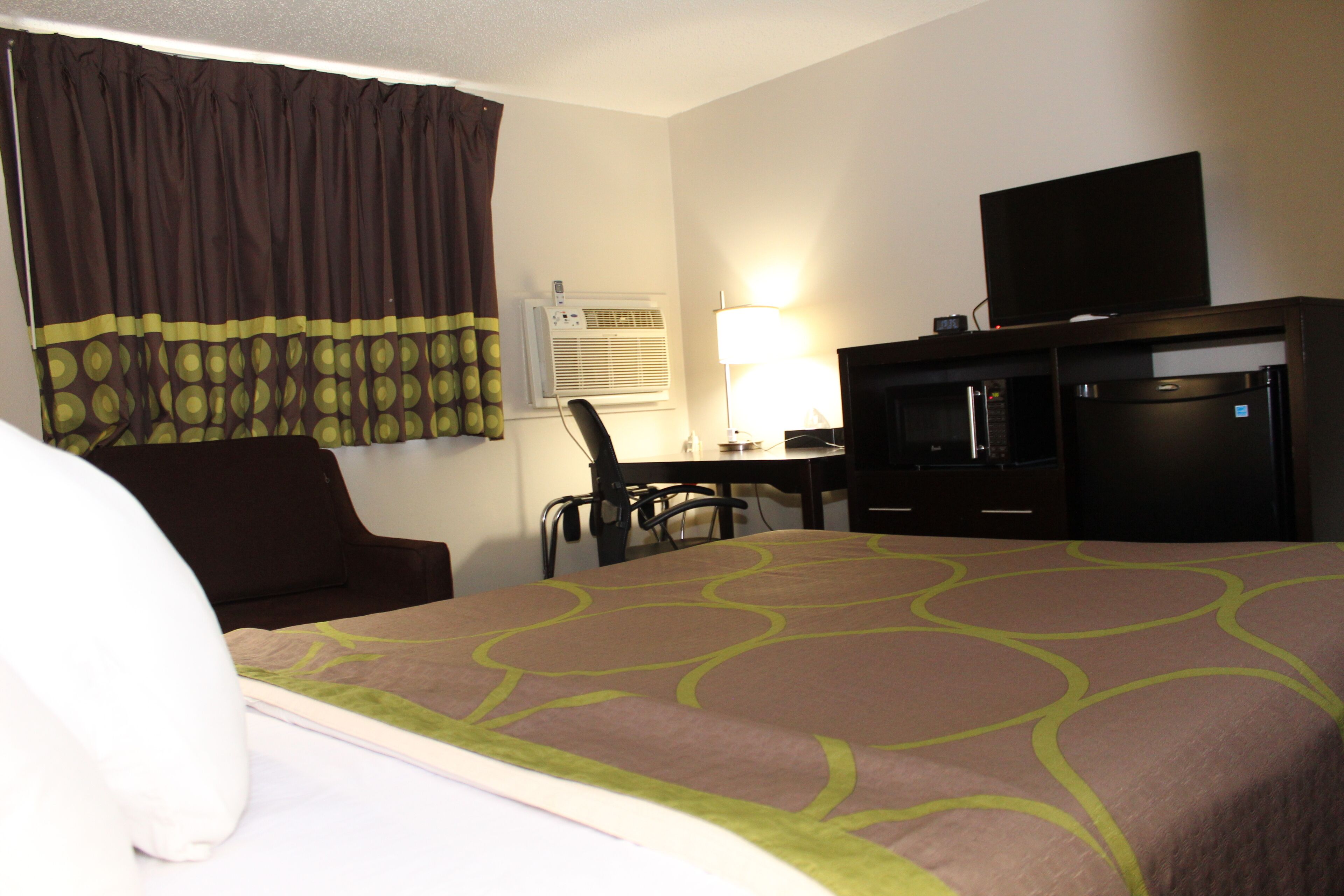 Quarto de hotel com cama, escrivaninha, cadeira, televisão e ar condicionado.
