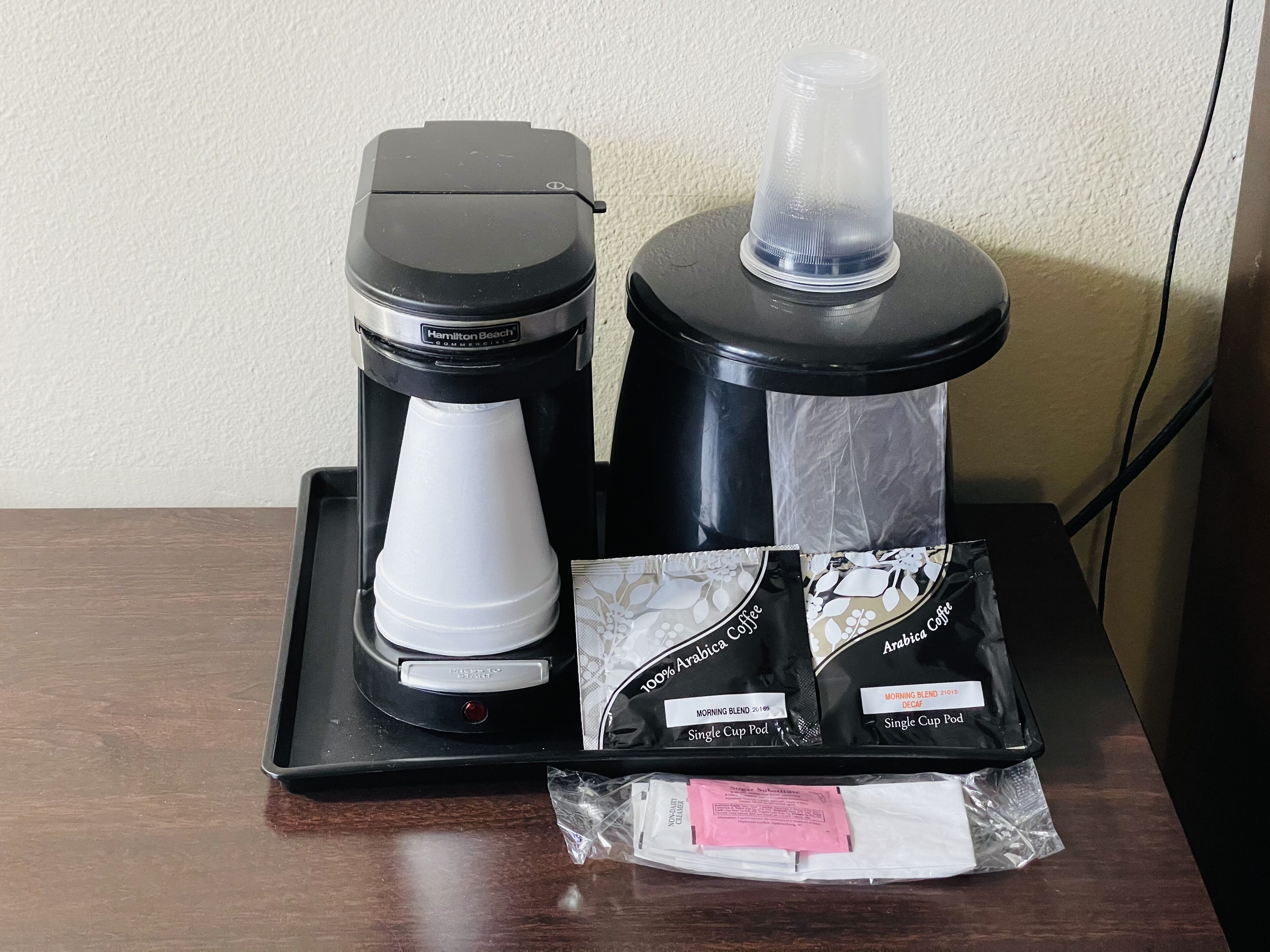 A coffee maker with a water reservoir and two coffee pods labeled "100% Arabica Coffee" and "Morning Blend 2019" on a tray.