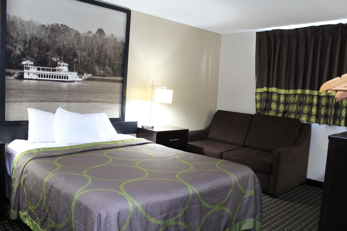 Une chambre d’hôtel comprenant un lit, un canapé, un bureau et une grande fenêtre donnant sur une rivière et des arbres.