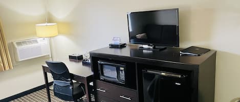 Une chambre d’hôtel équipée d’un bureau, d’une chaise, d’une télévision, d’un four à micro-ondes et d’une poubelle.