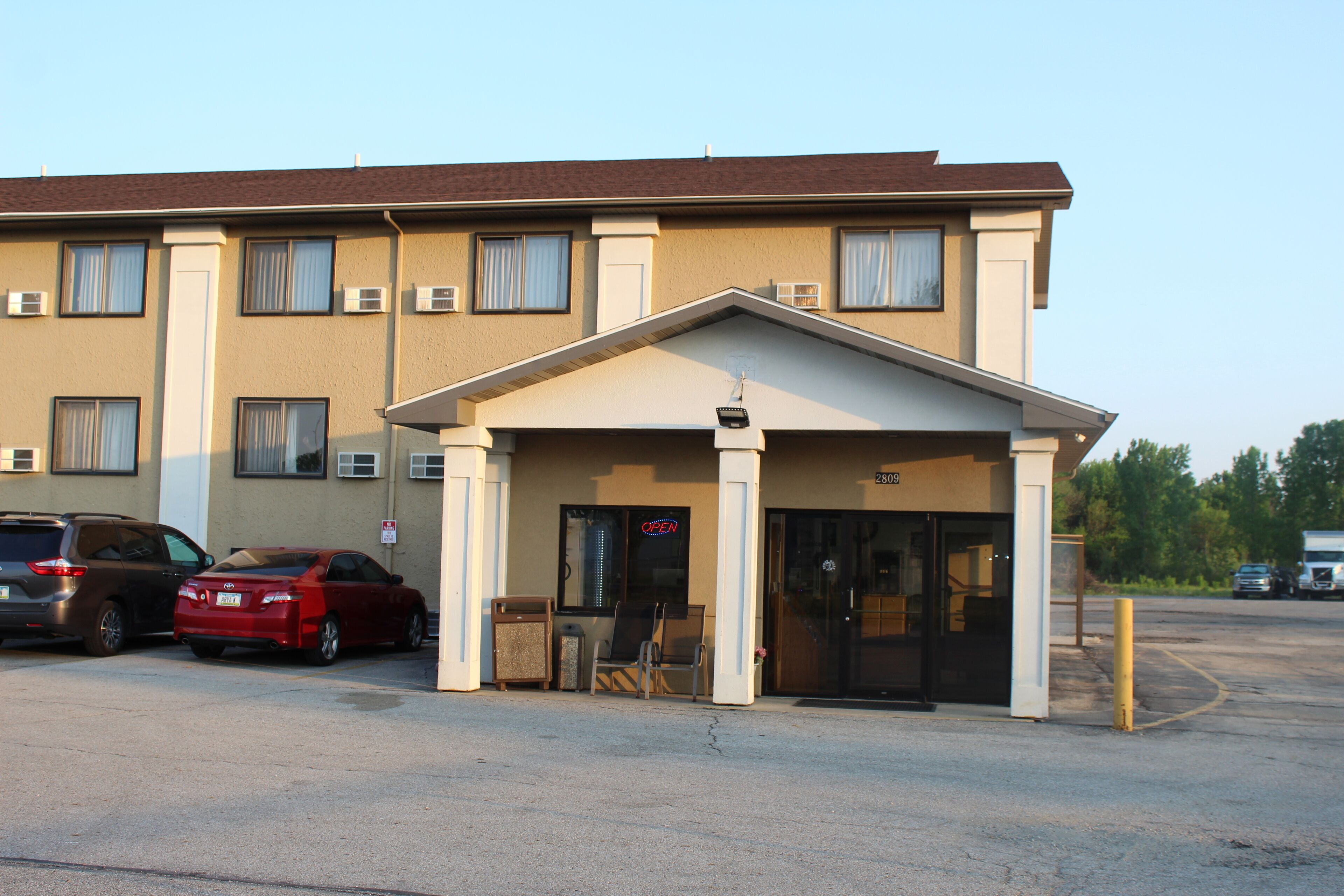 Un motel con entrada cubierta, estacionamiento y un edificio con múltiples ventanas y unidades de aire acondicionado.