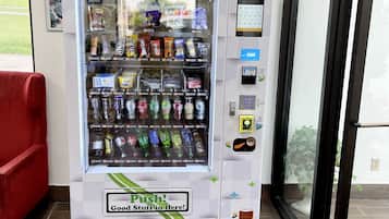 A vending machine stocked with snacks and drinks, located in a room with a red chair and a door leading outside.