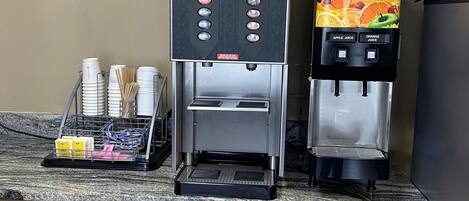 Ein Kaffee-Bereich mit einer Nescafe-Maschine, einem Saftspender und einem Schild mit den Frühstückszeiten.