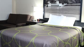 A hotel room with a bed, a nightstand, a lamp, and a poster of a boat on a lake.