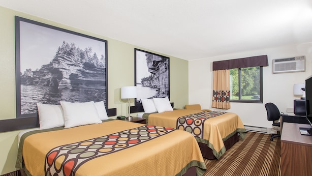 A hotel room with two beds, a desk, and a TV.
