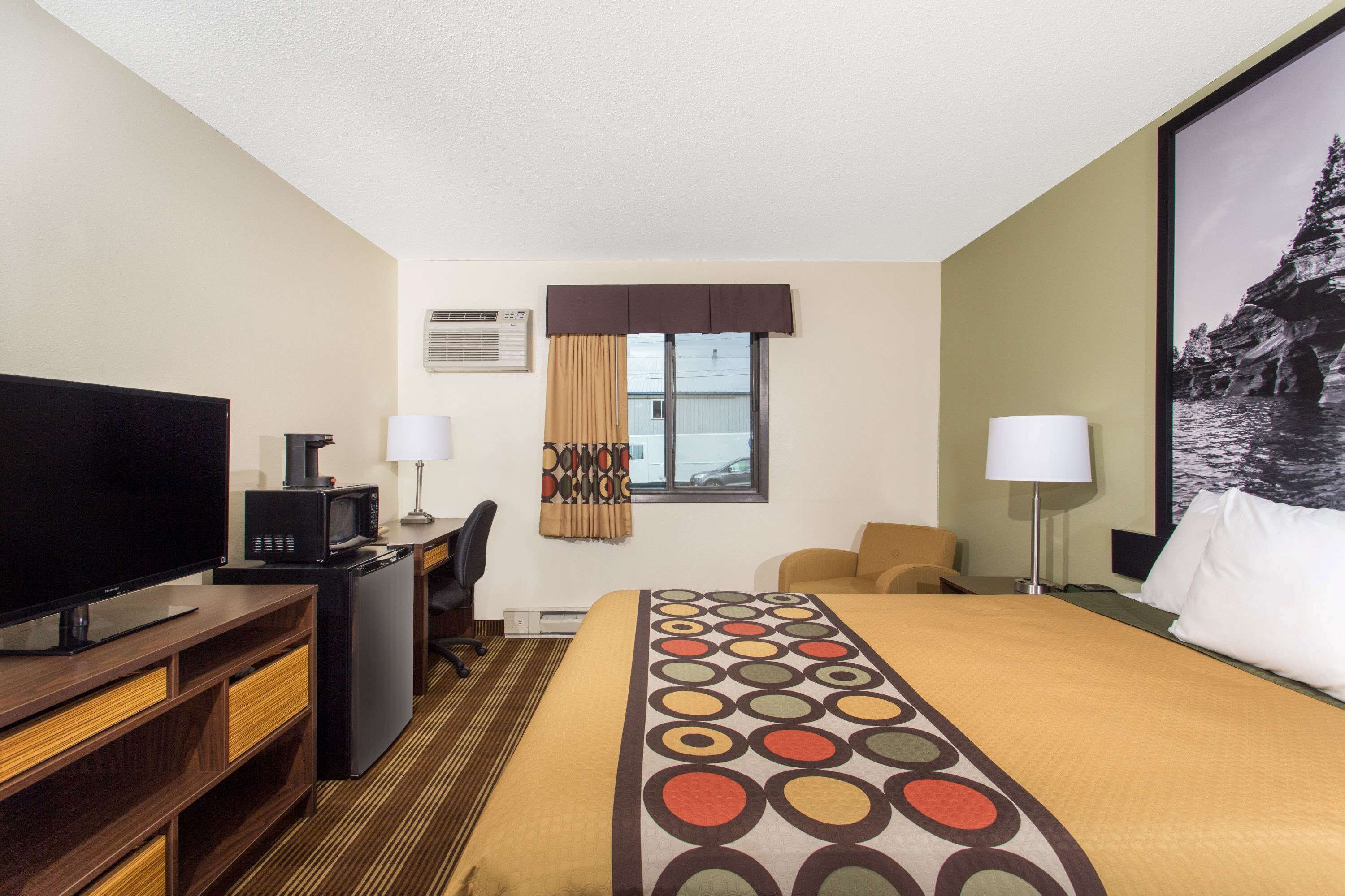 Habitación de hotel con una cama grande, un escritorio con computadora, un televisor y una ventana con cortinas.
