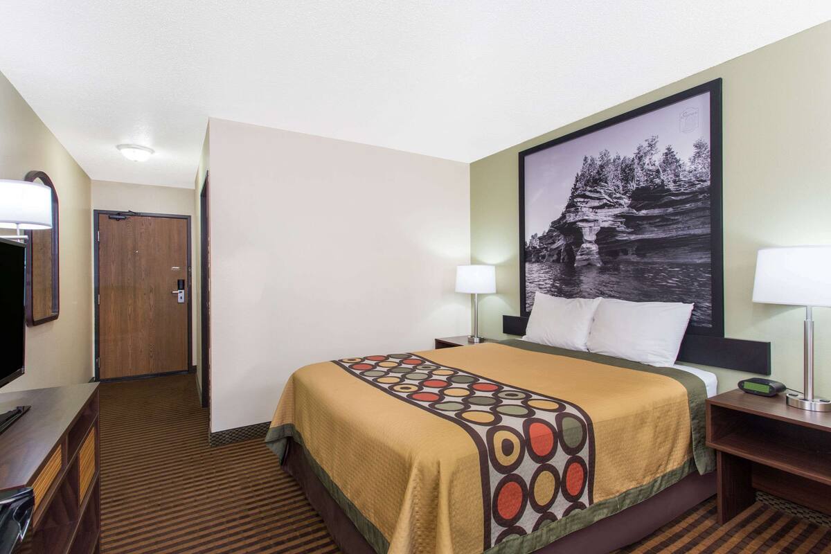 A hotel room with a bed, a TV, a desk, and a door.