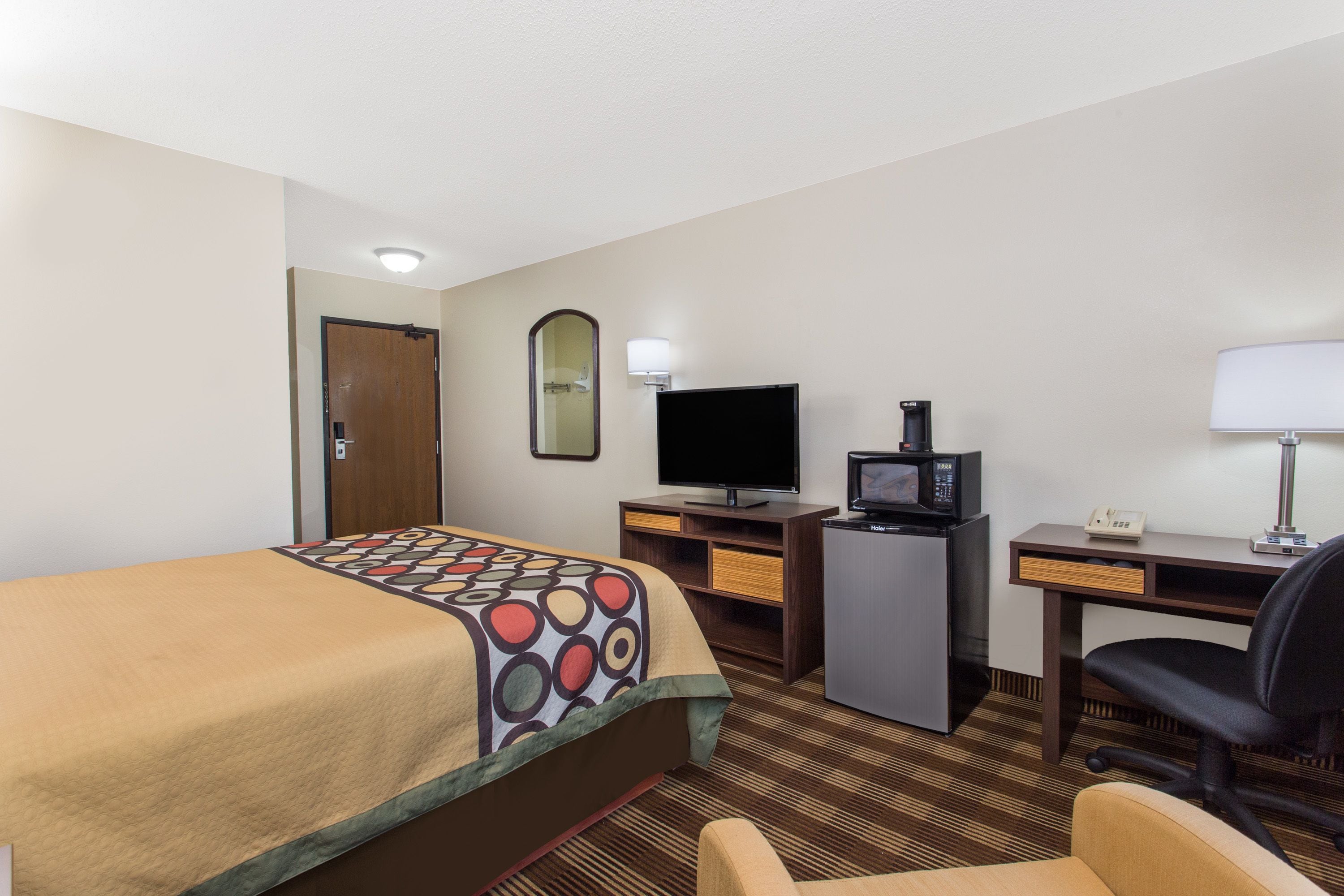 Una habitación de hotel con cama, escritorio, silla, televisión y un refrigerador pequeño.