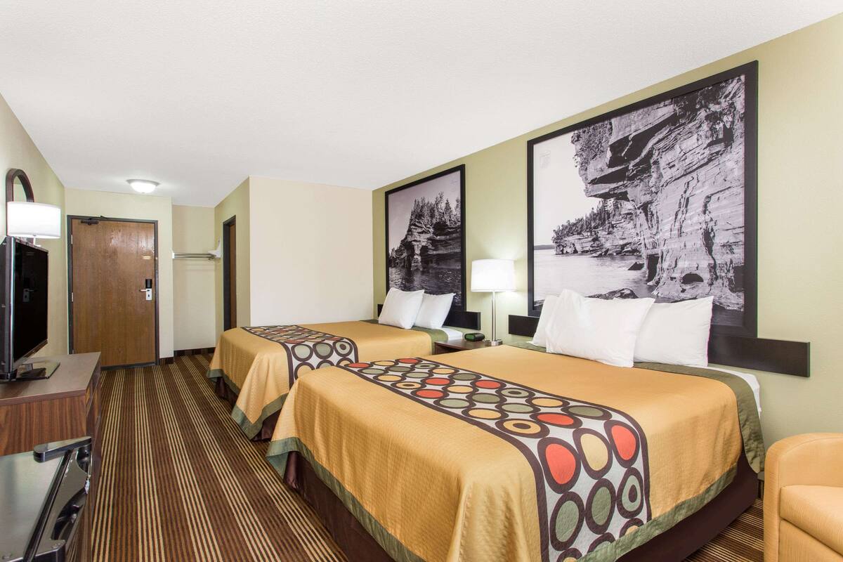 A hotel room with two beds, a TV, a desk, and a chair.