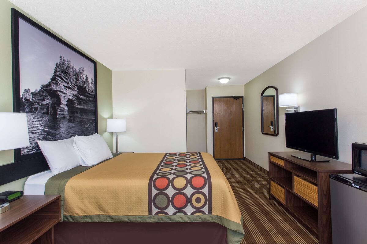 A hotel room with a bed, a television, a desk, and a mirror.