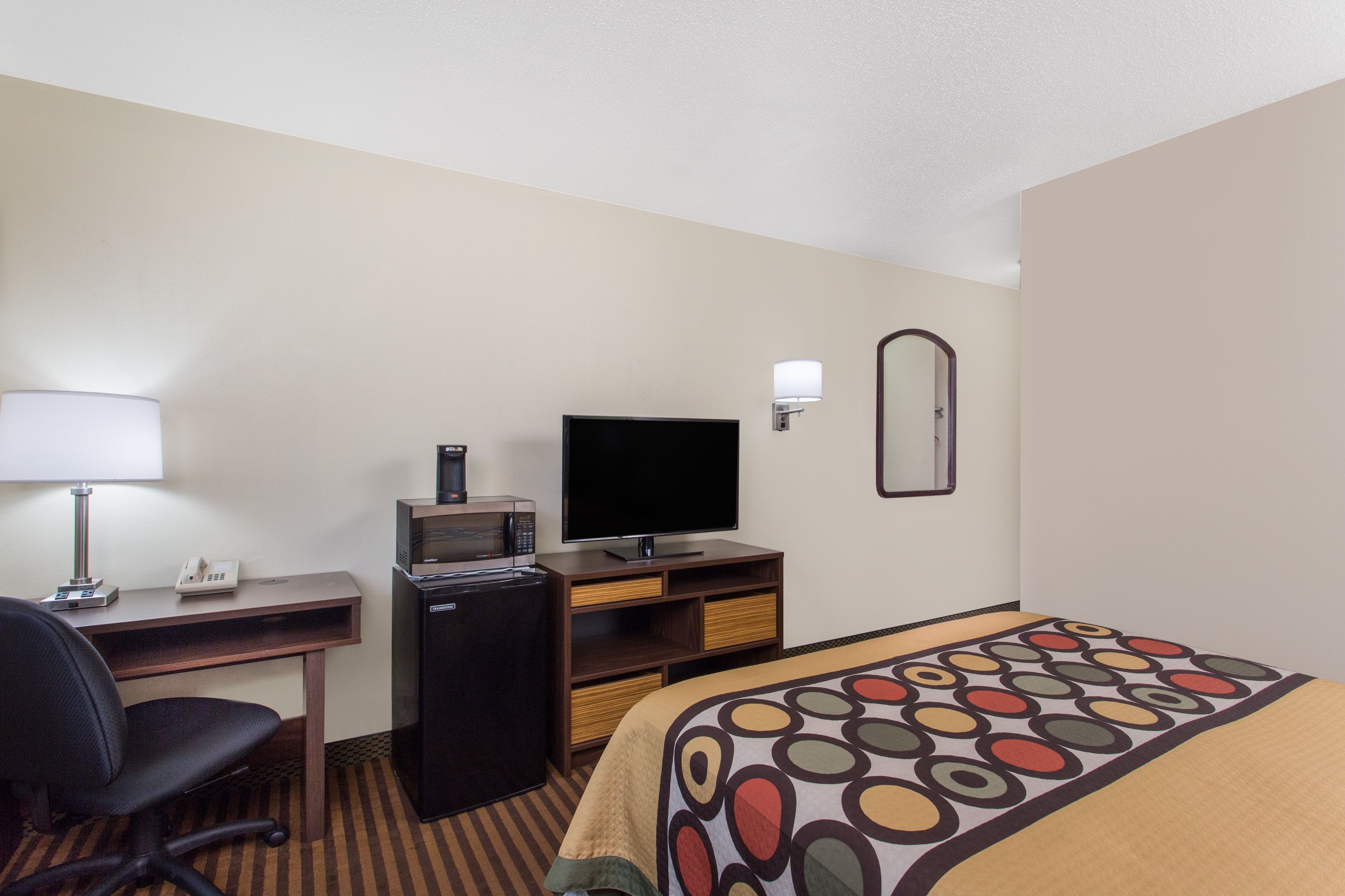 A hotel room with a bed, a desk, a chair, a television, a microwave, and a mirror.