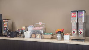 A self-service breakfast station with cereal dispensers, a coffee machine, and a bread display.