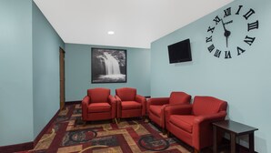 A room with teal walls, a large clock, three red chairs, a patterned carpet, and a waterfall painting.