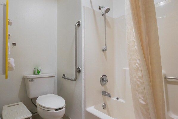 A bathroom with a toilet, a shower with grab bars, and a step stool.