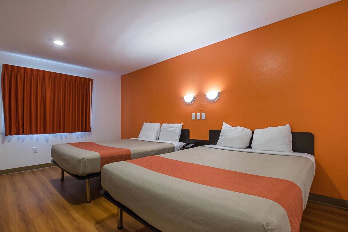 A hotel room with two beds, orange walls, and a window with curtains.