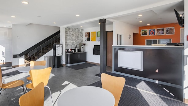 A modern hotel lobby with a reception desk, seating area, and a staircase. - Motel 6 Marshalltown, IA (Marshalltown)