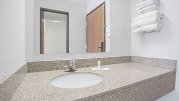 Une salle de bain avec un comptoir en granit, un lavabo blanc, un miroir et un porte-serviettes avec des serviettes pliées.