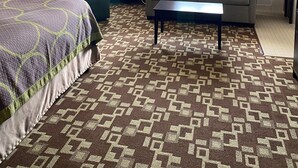 Une chambre d’hôtel avec un lit, un canapé, une table basse, une lampe et une grande fenêtre avec des rideaux.