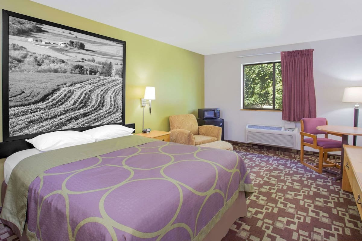 A hotel room with a bed, a desk, a chair, a TV, and a window with curtains.