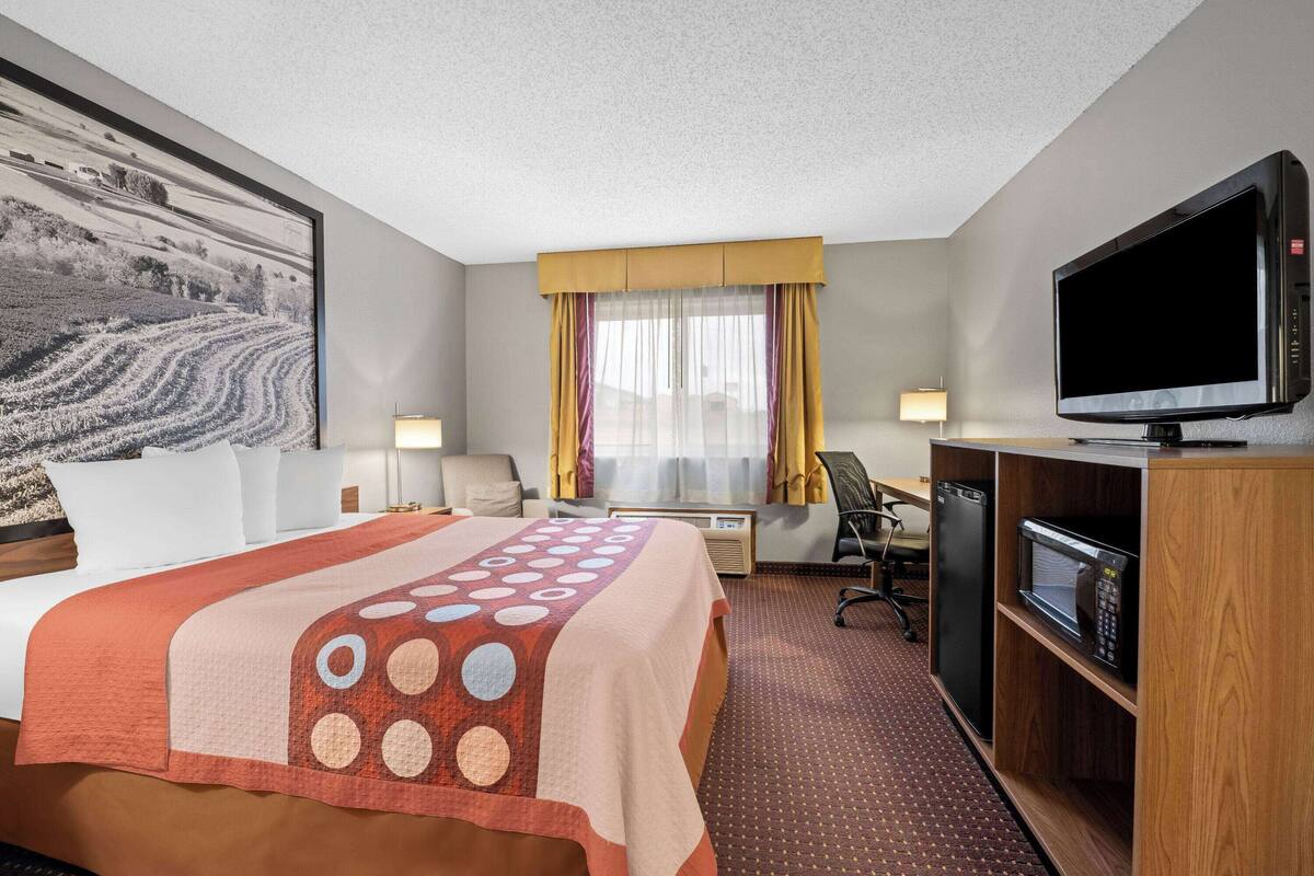 A hotel room with a bed, a television, a desk, a microwave, and a large window with curtains.