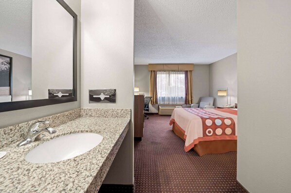 A hotel room with a granite countertop sink, a bed with a patterned bedspread, and a large mirror. - Super 8 by Wyndham Waverly (Waverly)