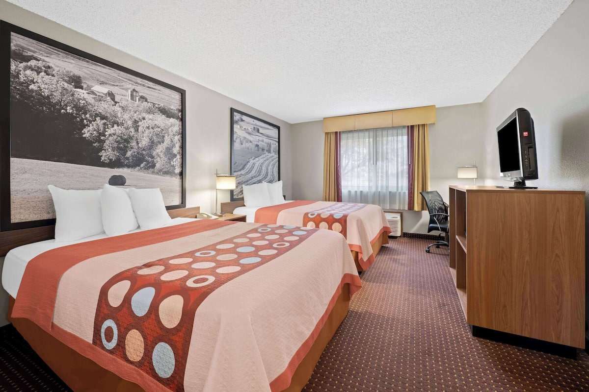 A hotel room with two beds, a desk, a television, and a large framed picture on the wall.