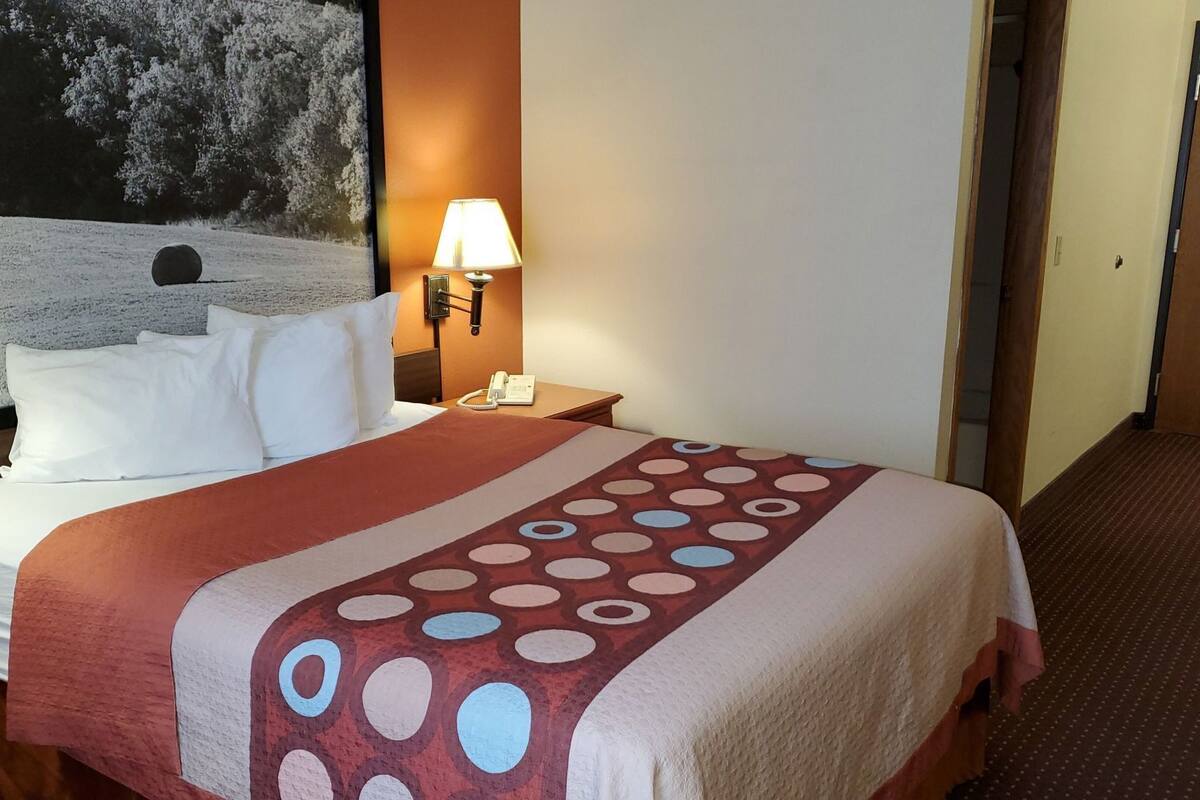 A hotel room with a bed, a nightstand, a lamp, and a painting on the wall.