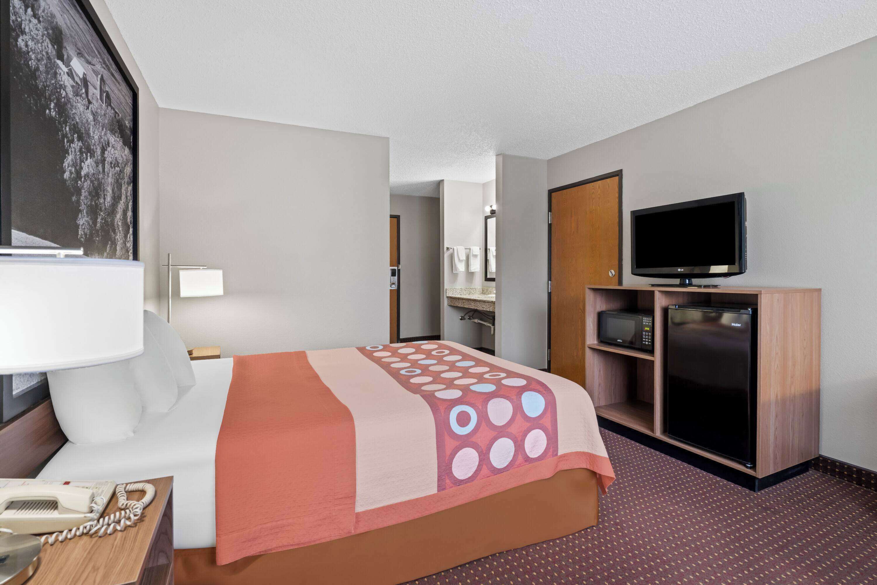 A hotel room with a bed, a TV, a microwave, and a refrigerator.