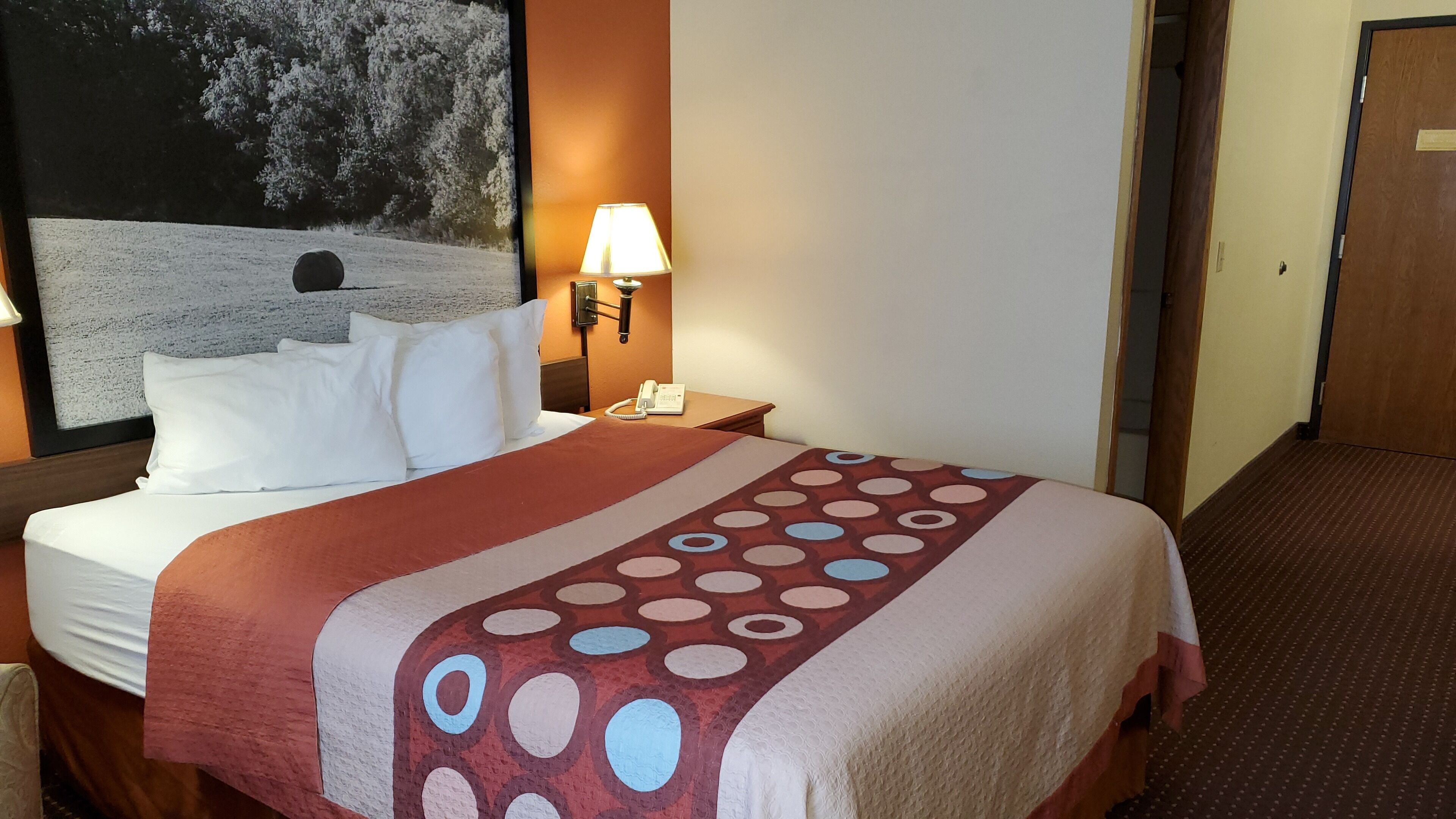 Ein Hotelzimmer mit Bett, Nachttisch mit Lampe, Telefon und einem Bild an der Wand.