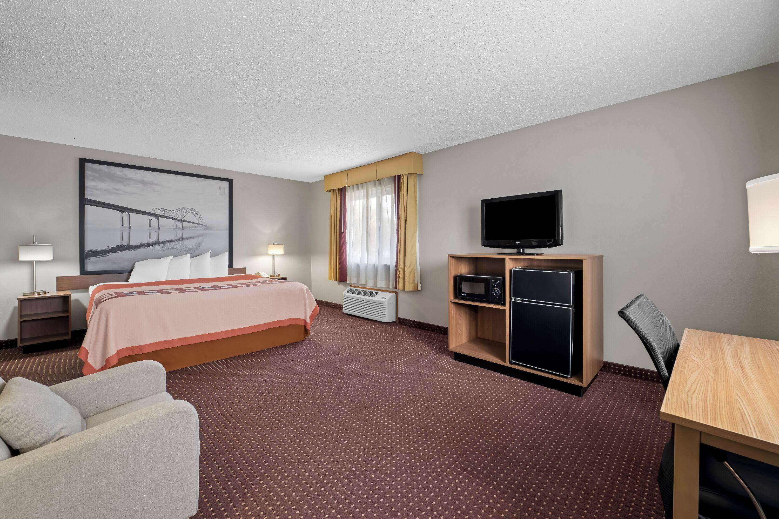 A hotel room with a bed, a desk, a television, and a large window with curtains.