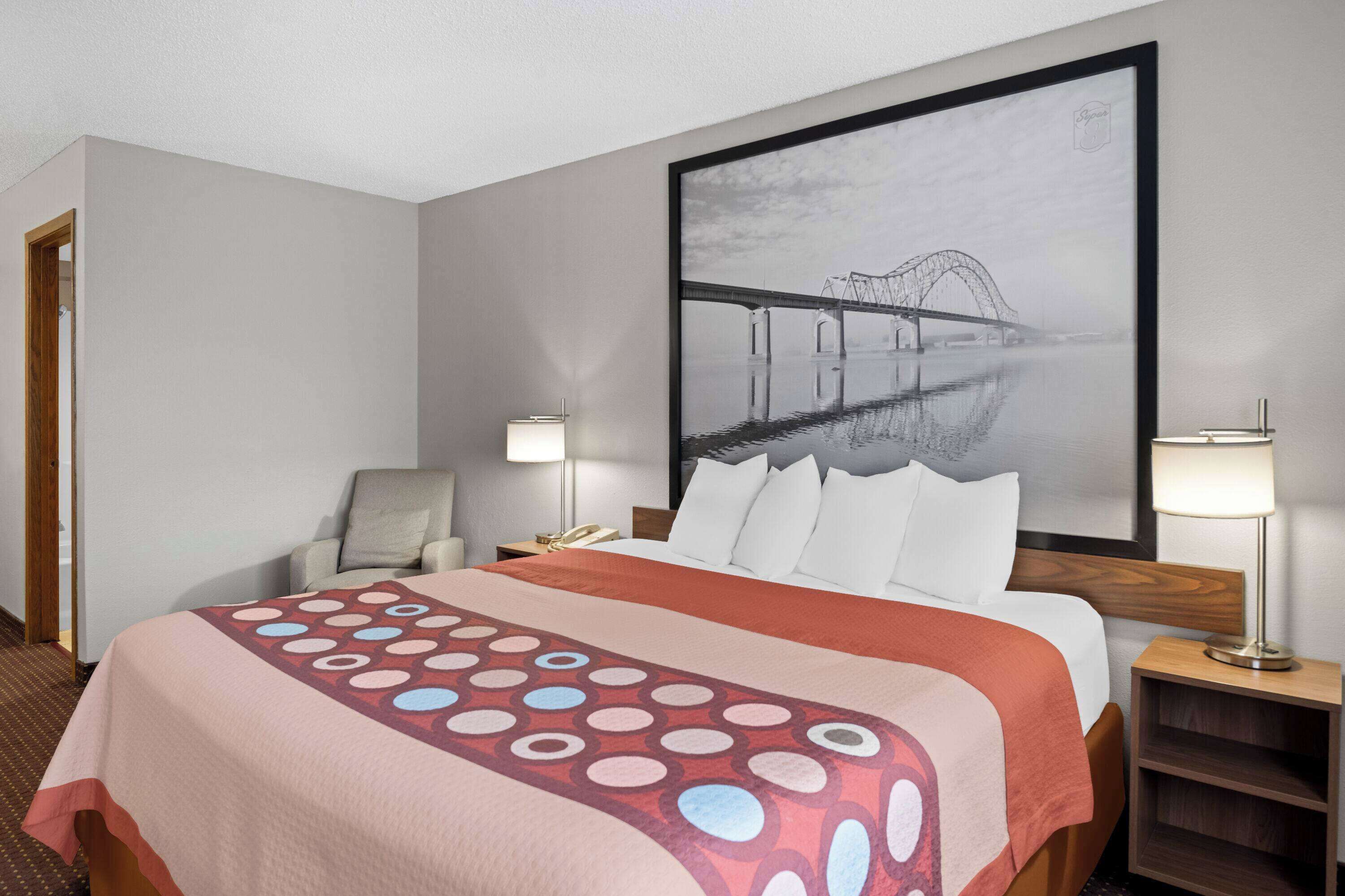 A hotel room with a large bed, a chair, a desk, and a wall-mounted TV.