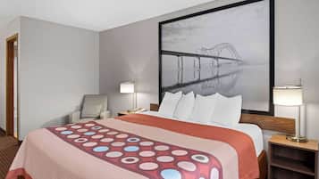 A hotel room with a large bed, a chair, a desk, and a wall-mounted TV.