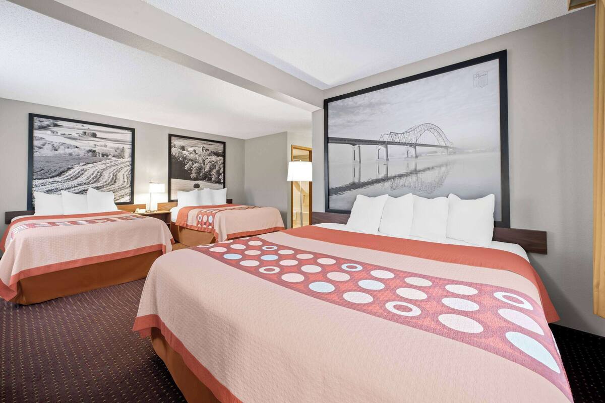 A hotel room with two beds, a large window, and artwork on the walls.