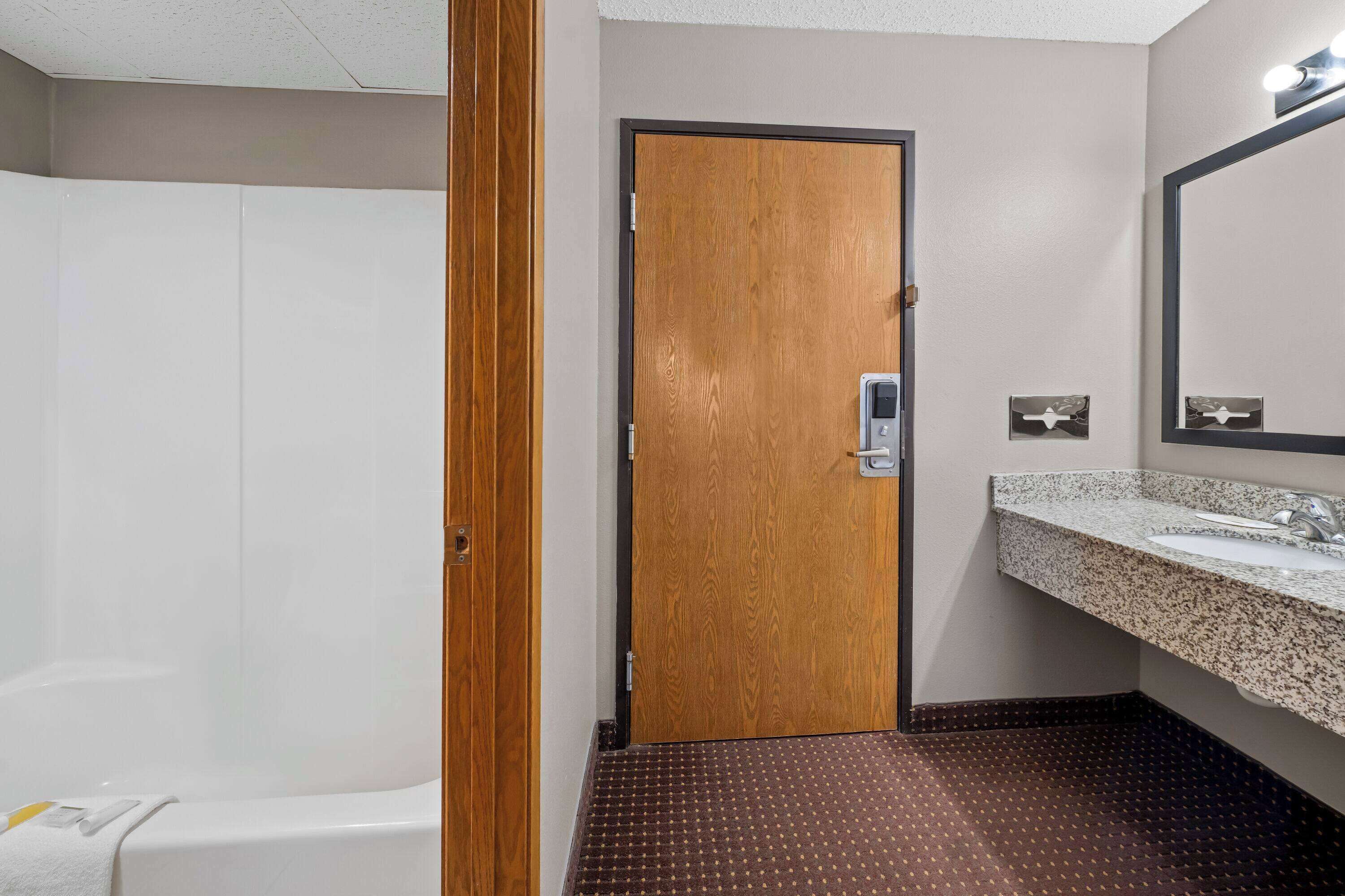 A bathroom with a wooden door, a sink with a granite countertop, and a shower area.