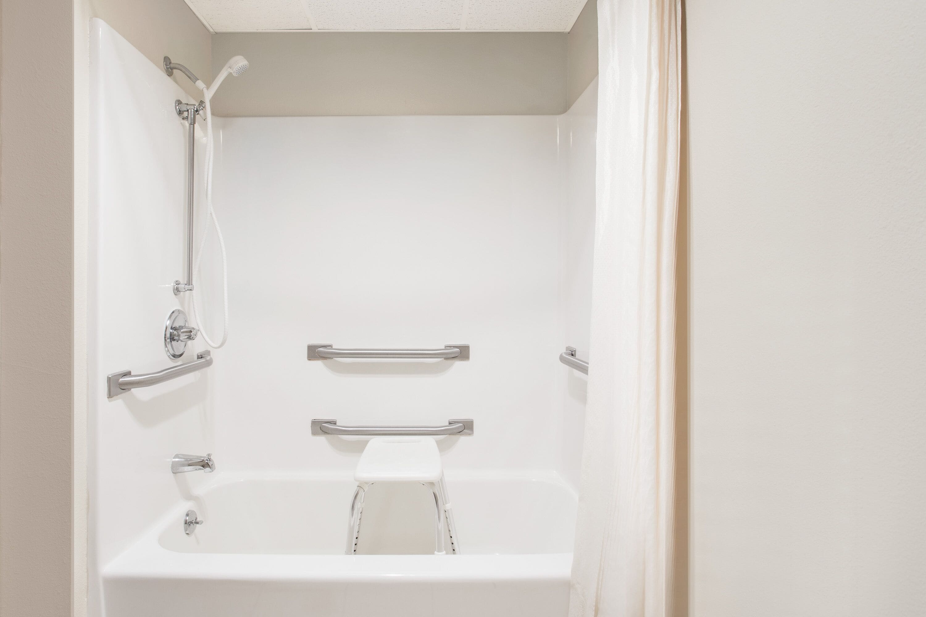 A modern bathroom with a bathtub, shower, and grab bars.