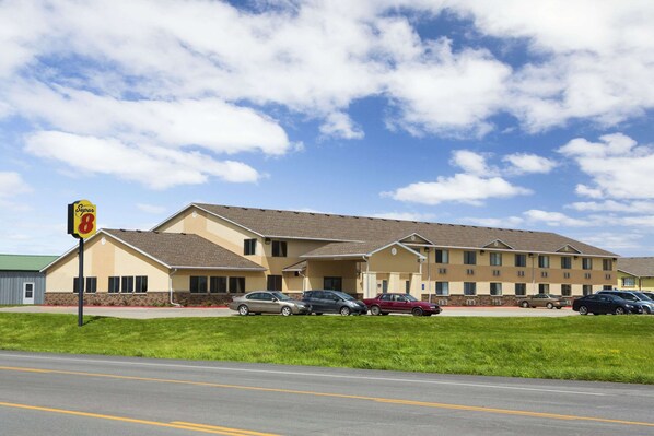 A motel with a two-story building, a parking lot with several cars, and a grassy area in front.