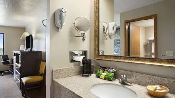 A hotel bathroom with a sink, mirror, towel dispenser, and a chair.