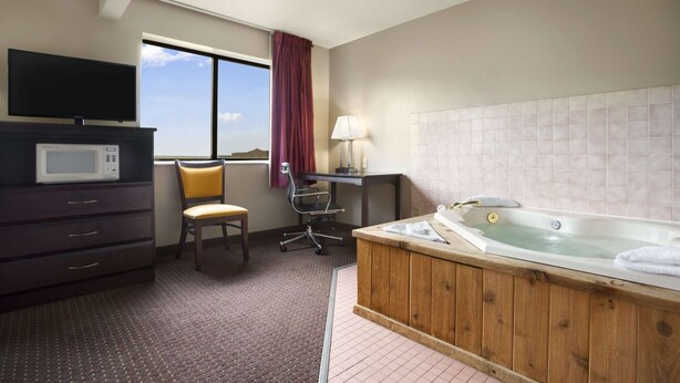 Un baño de hotel con una bañera de madera, un escritorio con lámpara, una silla, un televisor y un microondas.