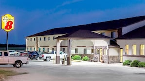 A Super 8 motel with a covered parking area and multiple vehicles parked outside. - Western Inn & Suites (Grinnell)