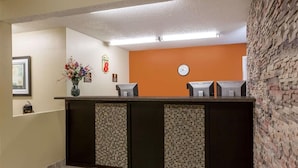 A reception desk with a clock, a vase of flowers, and a sign on the wall. - Western Inn & Suites (Grinnell)