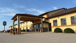 A Western Inn & Suites with a covered entrance, brick facade, and a parking lot with several cars. - Western Inn & Suites (Grinnell)