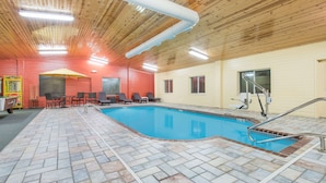 An indoor swimming pool with tiled flooring, wooden ceiling, and a poolside seating area with chairs and a table. - Super 8 by Wyndham Webster City IA (Webster City)